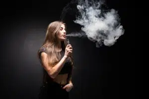 jeune-femme-sexy-vapote-fumant-cigarette-electronique-nuage-vapeur-mur-noir