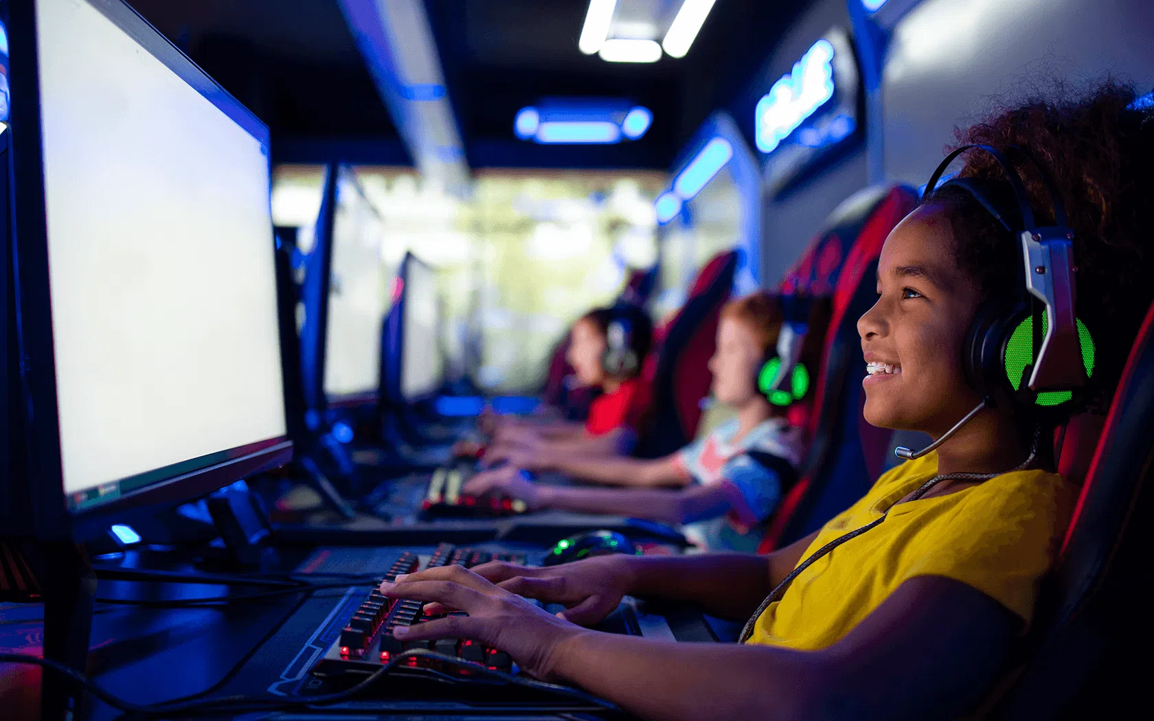 Enfants jouant à des jeux vidéo sur ordinateurs dans une salle de gaming avec casques et écrans lumineux.