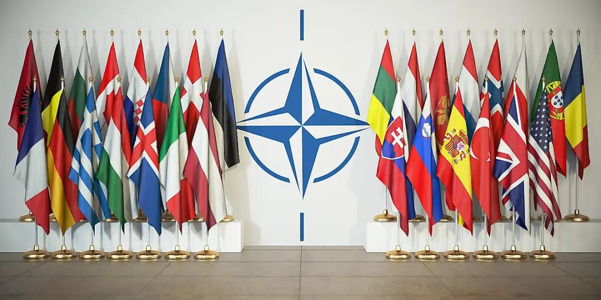 Drapeaux des pays membres de l’OTAN devant le logo de l’Alliance atlantique lors d’un sommet international.
