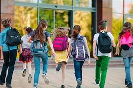 Groupe d’enfants avec des sacs à dos entrant dans une école lors de la rentrée scolaire.
