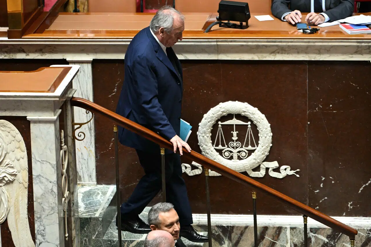 Un homme en costume descend les marches de l’Assemblée nationale, tenant des documents à la main.