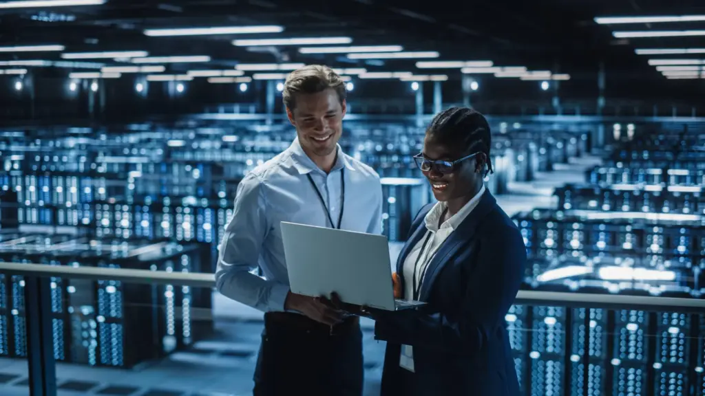 Deux professionnels en cybersécurité analysant des données sur un ordinateur portable dans un centre de serveurs moderne.
