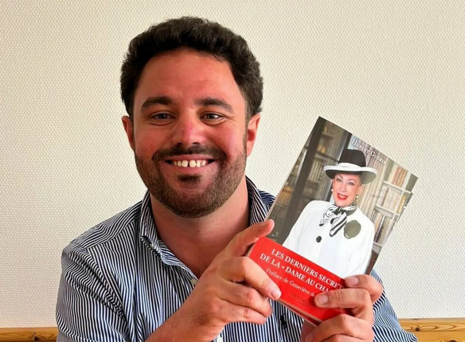 Hubert Guérin souriant, tenant son livre Les derniers secrets de la Dame au chapeau avec une photo de Geneviève de Fontenay en couverture