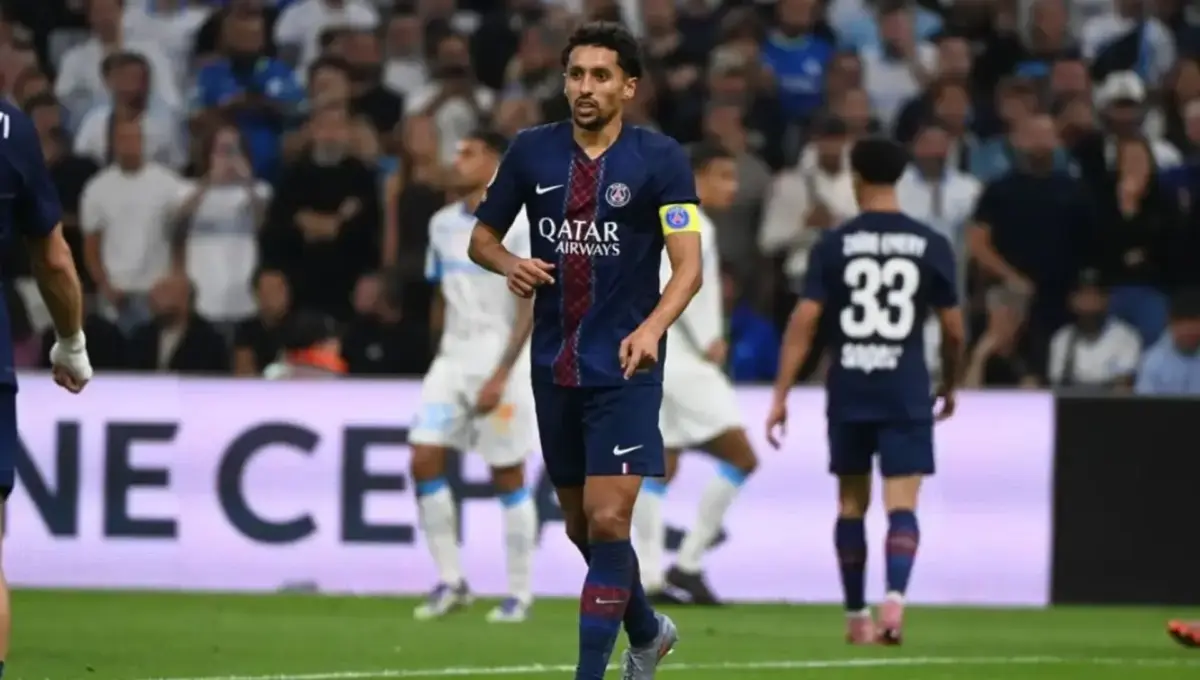 Joueur du PSG portant le brassard de capitaine sur le terrain lors d’un match de Ligue 1 contre Marseille, entouré de coéquipiers et d’adversaires, avec des supporters flous en arrière-plan.