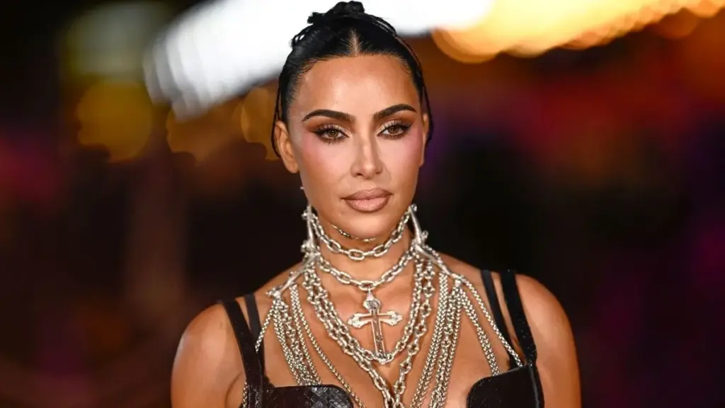 Kim Kardashian portant une robe noire et plusieurs colliers argentés superposés lors d’un événement public.