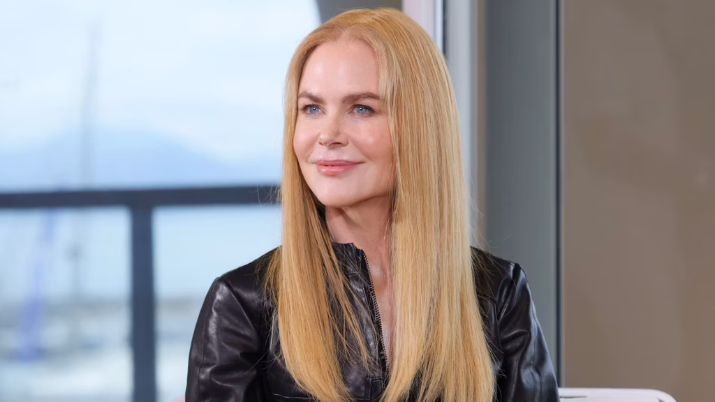 Femme aux cheveux blonds lisses portant une veste en cuir noir, assise près d’une fenêtre lumineuse.