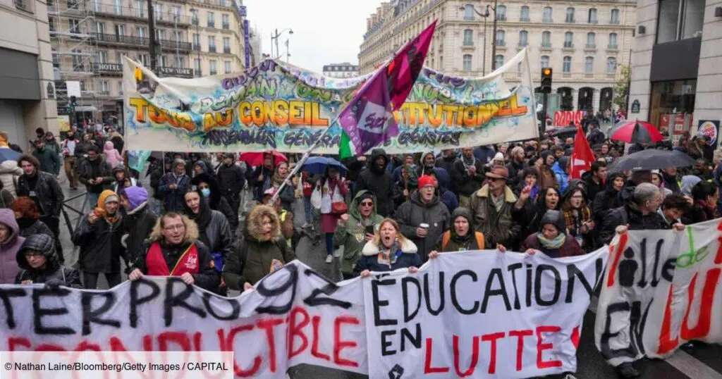 Manifestation dans les rues de Paris avec une foule nombreuse tenant des banderoles, dont "Tous au Conseil Constitutionnel" et "Education en lutte", devant des immeubles haussmanniens par temps pluvieux.