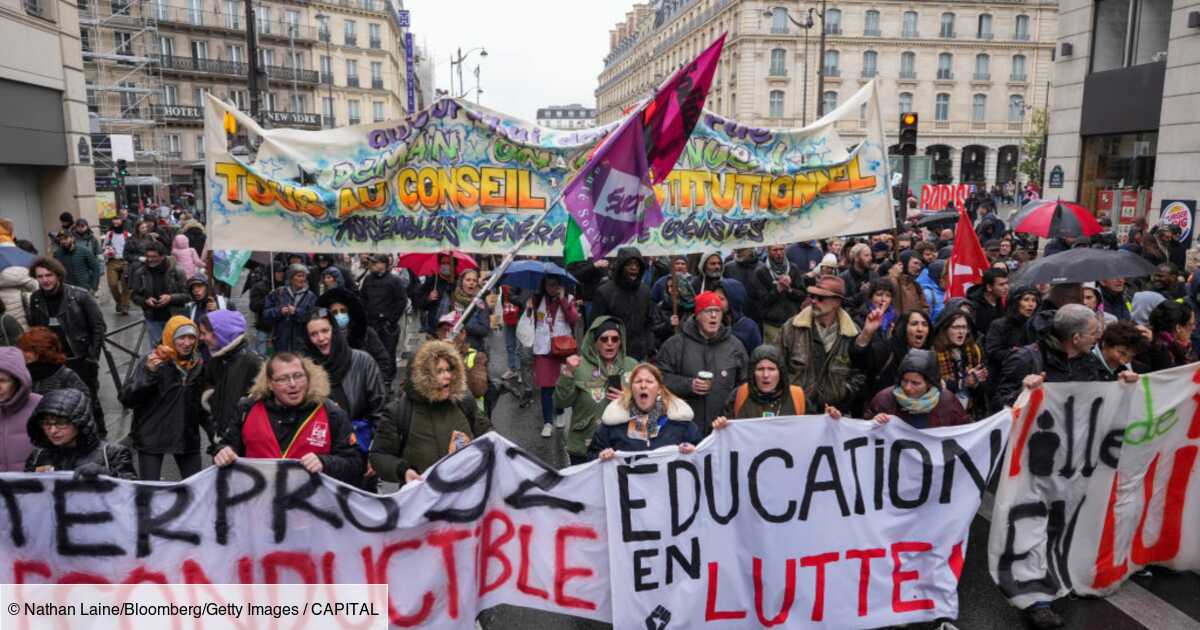 Manifestation dans les rues de Paris avec une foule nombreuse tenant des banderoles, dont "Tous au Conseil Constitutionnel" et "Education en lutte", devant des immeubles haussmanniens par temps pluvieux.