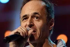 Chanteur français interprétant une chanson sur scène, micro à la main.