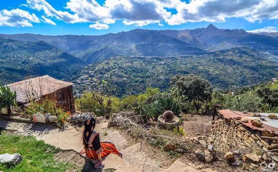 Paysage des montagnes de Kabylie avec une femme en tenue traditionnelle assise au premier plan.