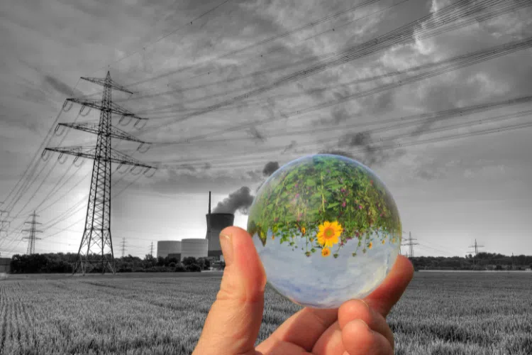 Main tenant une sphère montrant un paysage naturel coloré devant une centrale électrique et des lignes haute tension en noir et blanc, symbolisant la transition énergétique.