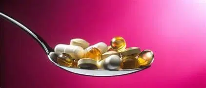 Cuillère contenant plusieurs compléments alimentaires sous forme de gélules et de capsules, illustrant la supplémentation nutritionnelle.