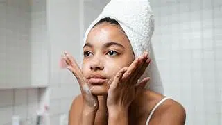 Jeune femme appliquant un soin hydratant sur le visage devant un miroir, illustrant une routine skincare et le principe du skin cycling.