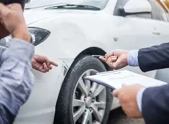 Deux personnes examinent une voiture endommagée avec un bloc-notes, lors d’une expertise automobile après sinistre.