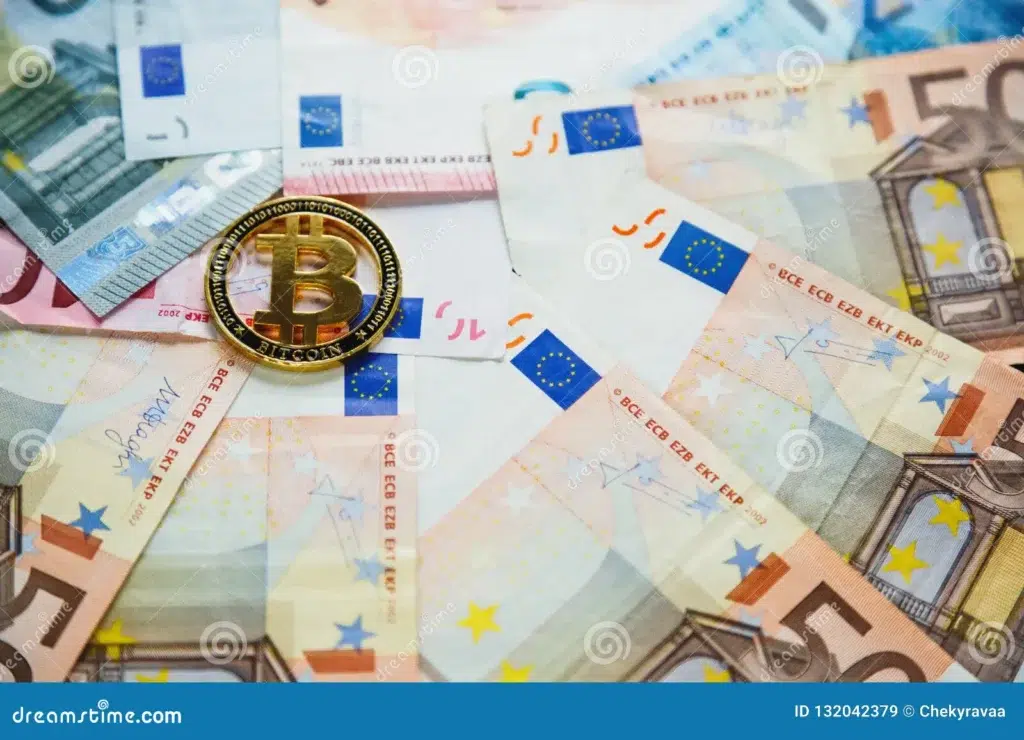 Pièce de Bitcoin dorée posée sur des billets de 100 euros illustrant l'achat de cryptomonnaie avec un petit budget