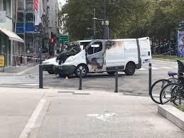 Fourgon blanc endommagé, flanc noirci, immobilisé au milieu d’un carrefour en ville.
