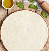 Pâte à pizza maison étalée en disque sur une planche, avec un rouleau à pâtisserie et un peu d’huile d’olive à côté.