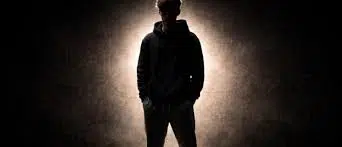 Silhouette sombre d’un jeune homme en sweat à capuche dans la pénombre