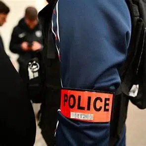 Brassard « POLICE » sur l’uniforme d’un agent, avec d’autres policiers en arrière-plan.
