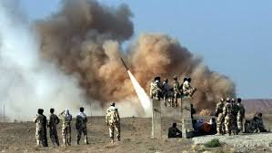 Des soldats observent un lancement de missile sur fond d’explosion et de fumée dans une zone désertique.