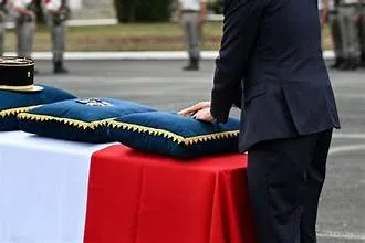 Un homme se recueille devant un cercueil recouvert d’un drapeau français lors d’une cérémonie militaire.