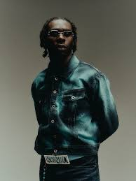 Kerchak pose sans sa cagoule, vêtu d’une tenue sombre brillante et de lunettes noires.