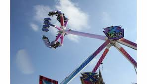 Un manège à sensations de type bras mécanique suspend des passagers en hauteur dans un parc d’attractions.