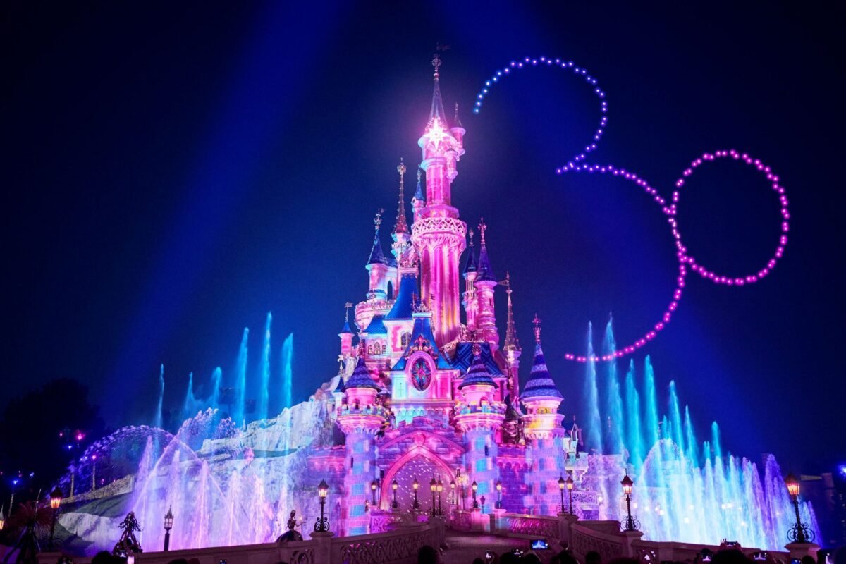 Le château de Disneyland Paris illuminé de couleurs roses et bleues lors d’un spectacle nocturne célébrant les 30 ans du parc.