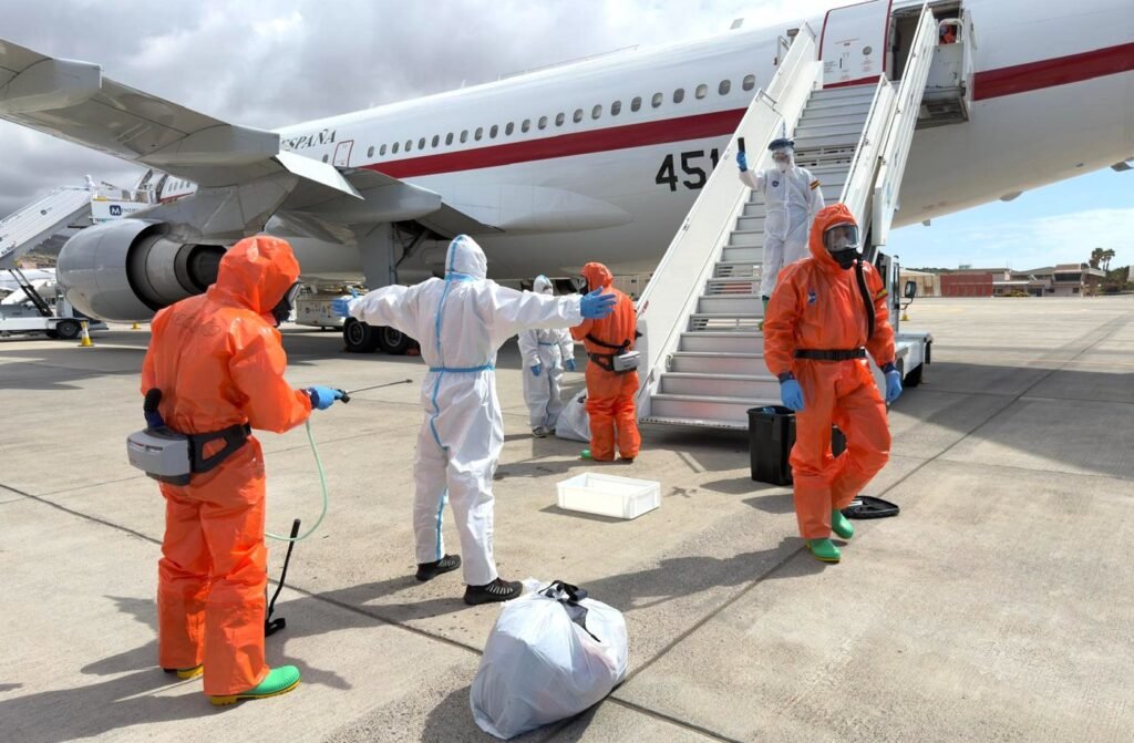 Équipes sanitaires en combinaison de protection autour d’un avion lors d’une opération de contrôle liée à un risque épidémique.