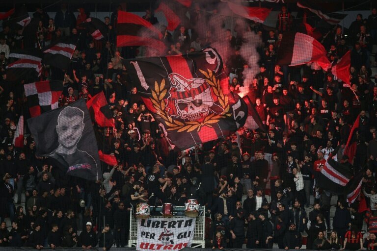 Tribune d’ultras de l’OGC Nice avec drapeaux rouge et noir, fumigènes et animations dans les tribunes lors d’un match de football.