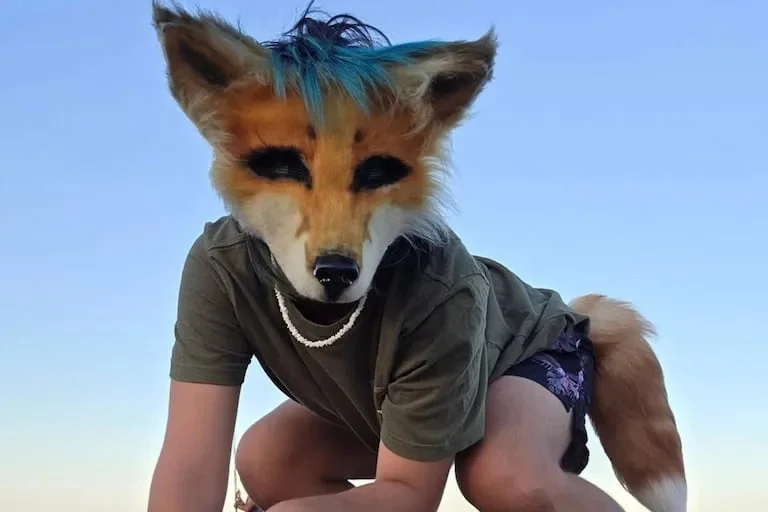 Enfant portant un masque inspiré d’un félin et une queue d’animal, se déplaçant à quatre pattes dans un espace vert dans le cadre d’une activité associée à la communauté therian.