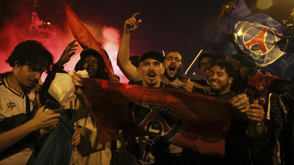 Supporters du PSG célébrant la victoire du club en Ligue des champions dans la nuit parisienne, avec drapeaux, fumigènes rouges et chants de fête.