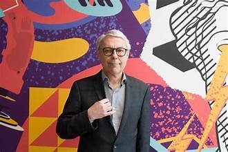 Homme en costume posant devant une fresque colorée, illustrant l’article consacré à la disparition d’un cofondateur d’Ubisoft.