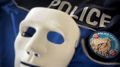 Masque blanc posé devant un uniforme de police et un écusson, illustrant une affaire de faux policiers liée à une tentative d’extorsion en cryptomonnaies.