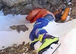 Corps d’un alpiniste équipé de bottes vertes, allongé dans la neige sur les pentes rocheuses de l’Everest.