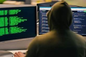 Personne encapuchonnée devant plusieurs écrans affichant du code informatique, illustrant une affaire de cybercriminalité et de vol massif de données.