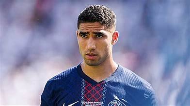 Joueur du PSG en maillot bleu, le regard sérieux, sur une pelouse de football.