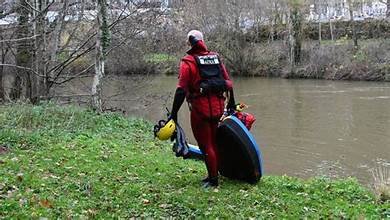 Un plongeur de la gendarmerie marche au bord d’une rivière avec son équipement, lors de recherches menées dans le cadre d’une disparition inquiétante.