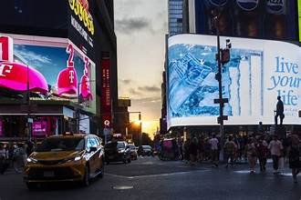 Vue de Times Square à New York avec ses écrans lumineux, ses taxis et de nombreux passants, illustrant une scène de panique après des coups de feu.