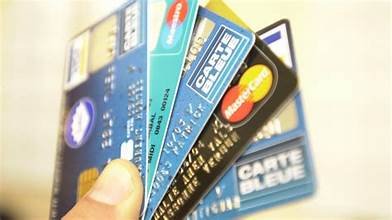 Main tenant plusieurs cartes bancaires, illustrant une affaire de retraits et d’achats frauduleux réalisés avec la carte d’un retraité.