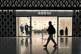 Boutique Gucci éclairée dans un centre commercial, avec une silhouette passant devant la vitrine.