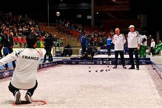 Joueurs de pétanque portant les couleurs de la France lors d’une compétition disputée devant des tribunes remplies.