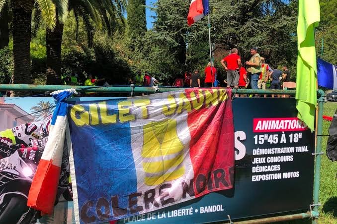 Bannière des Gilets jaunes installée à Bandol, avec des drapeaux français et des manifestants en arrière-plan.