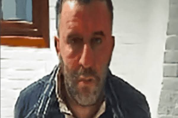 Homme recherché en Belgique, photographié de face, avec une barbe et une veste sombre.
